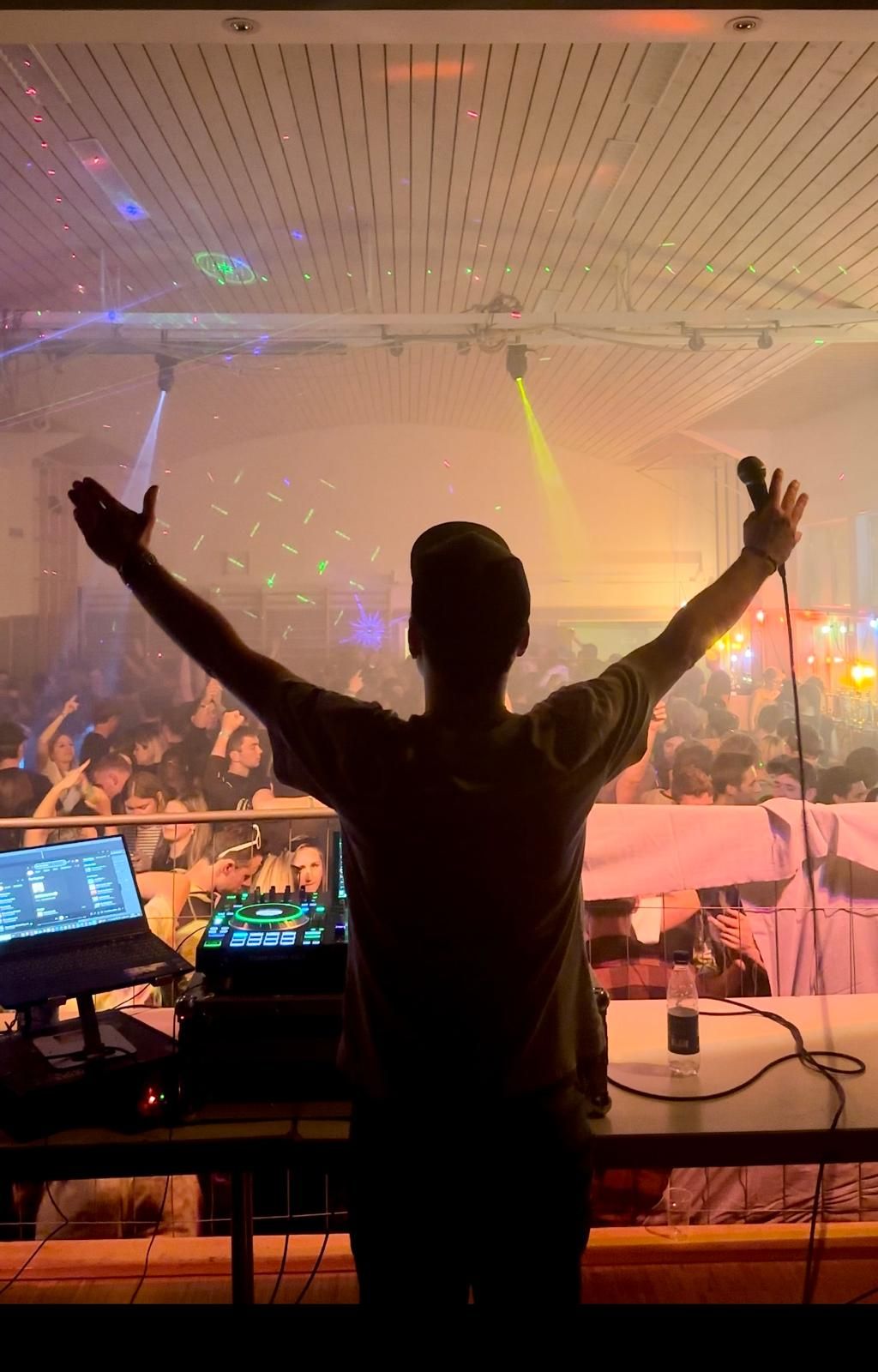 DJ Jouhännes steht mit ausgebreiteten Armen vor einer vollen Tanzfläche bei einem Fest in Vorarlberg